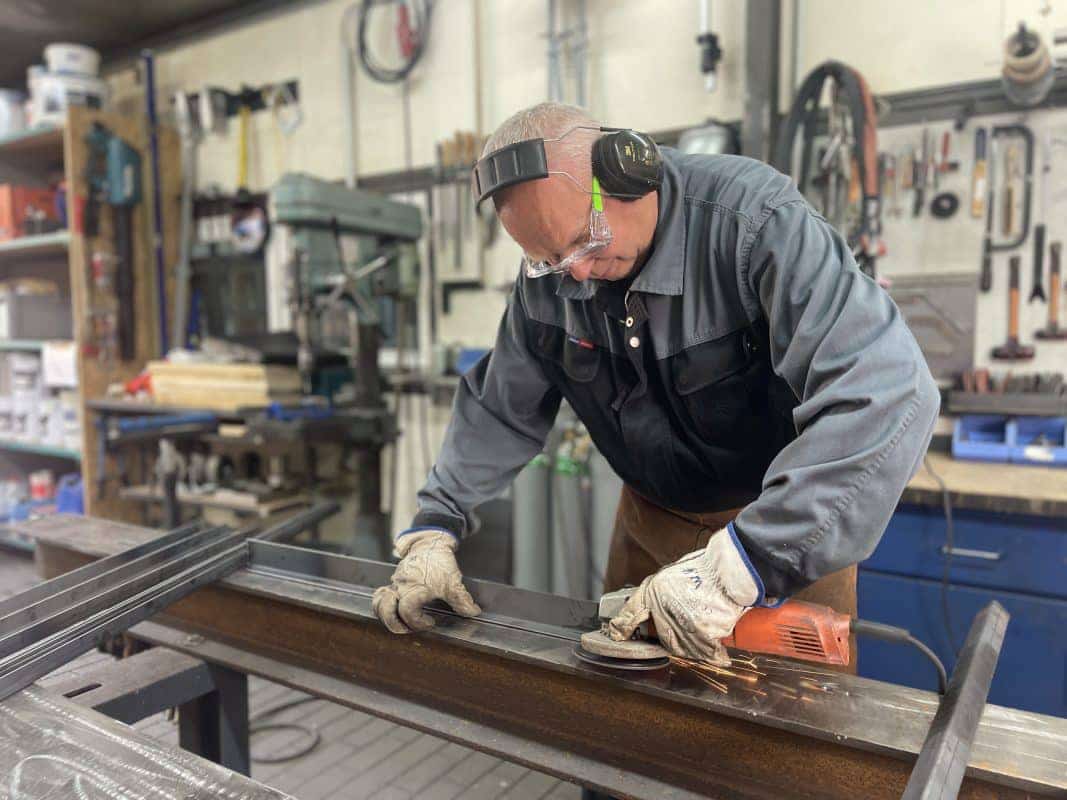 Person schleift Metallrahmen in der Werkstatt, Funken fliegen vom Werkzeug.