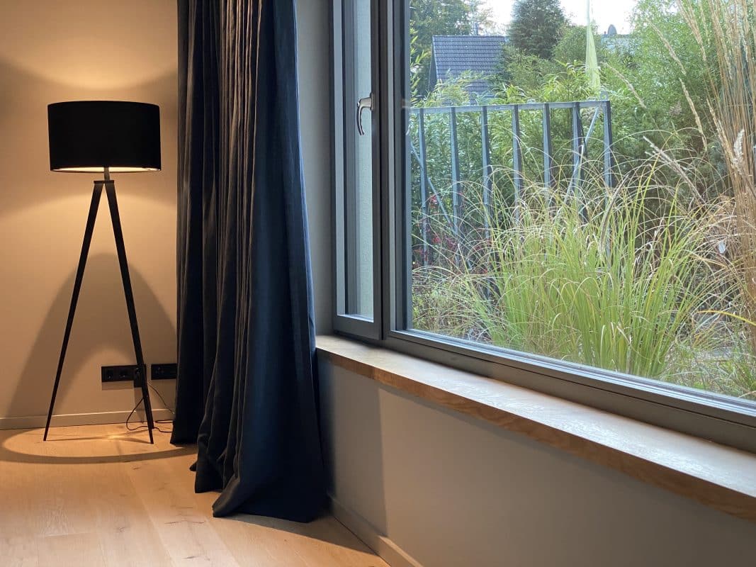 Fertige Holzfensterbank mit grüner Natur im Hintergrund und einer Stehlampe in der Ecke des Raumes.