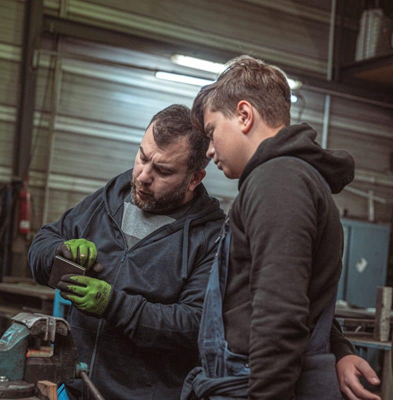 Zwei Werkstattmitarbeiter arbeiten gemeinsam an einem Metallteil in der Werkstatt.