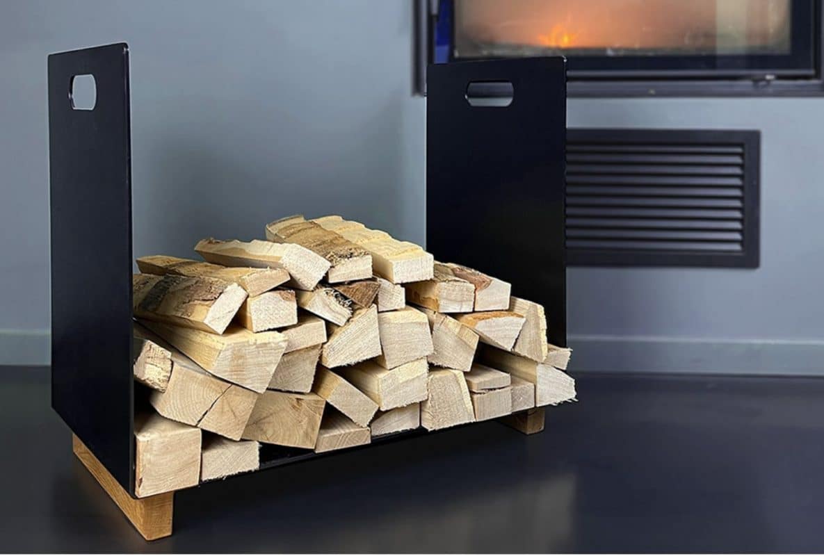 Kaminholzaufbewahrung aus schwarzem Metall und einer Eichenbasis steht gefüllt mit Holzscheiten vor dem Kamin.