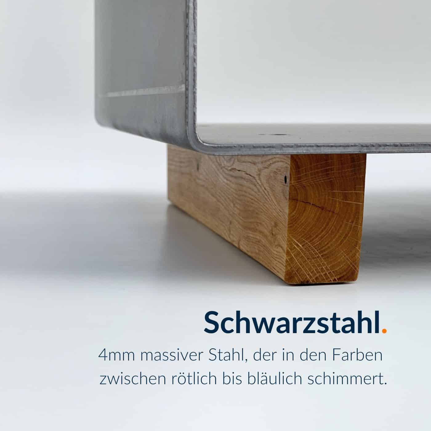Ein beschichteter Kaminholzständer aus Schwarzstahl steht auf einem Holzsockel.