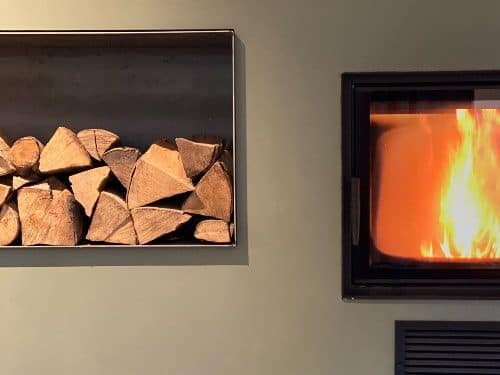 Kamin mit sichtbarer Flamme und Holzlagerung in Wandnische.