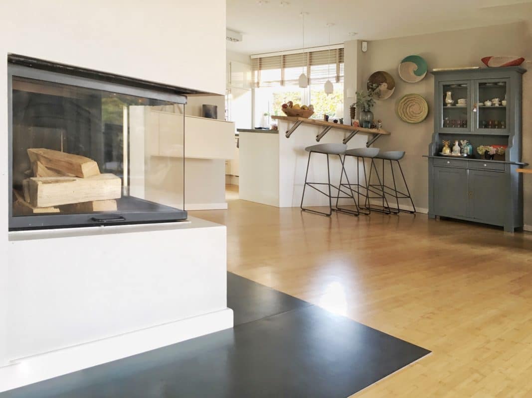 Funkenschutzplatte aus Metall vor einem modernen Kamin in einem hellen Wohnraum mit Holzboden.