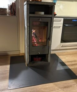 Ein Kamin steht auf einer dunklen Funkenschutz-Platte im Raum und brennt ruhig.