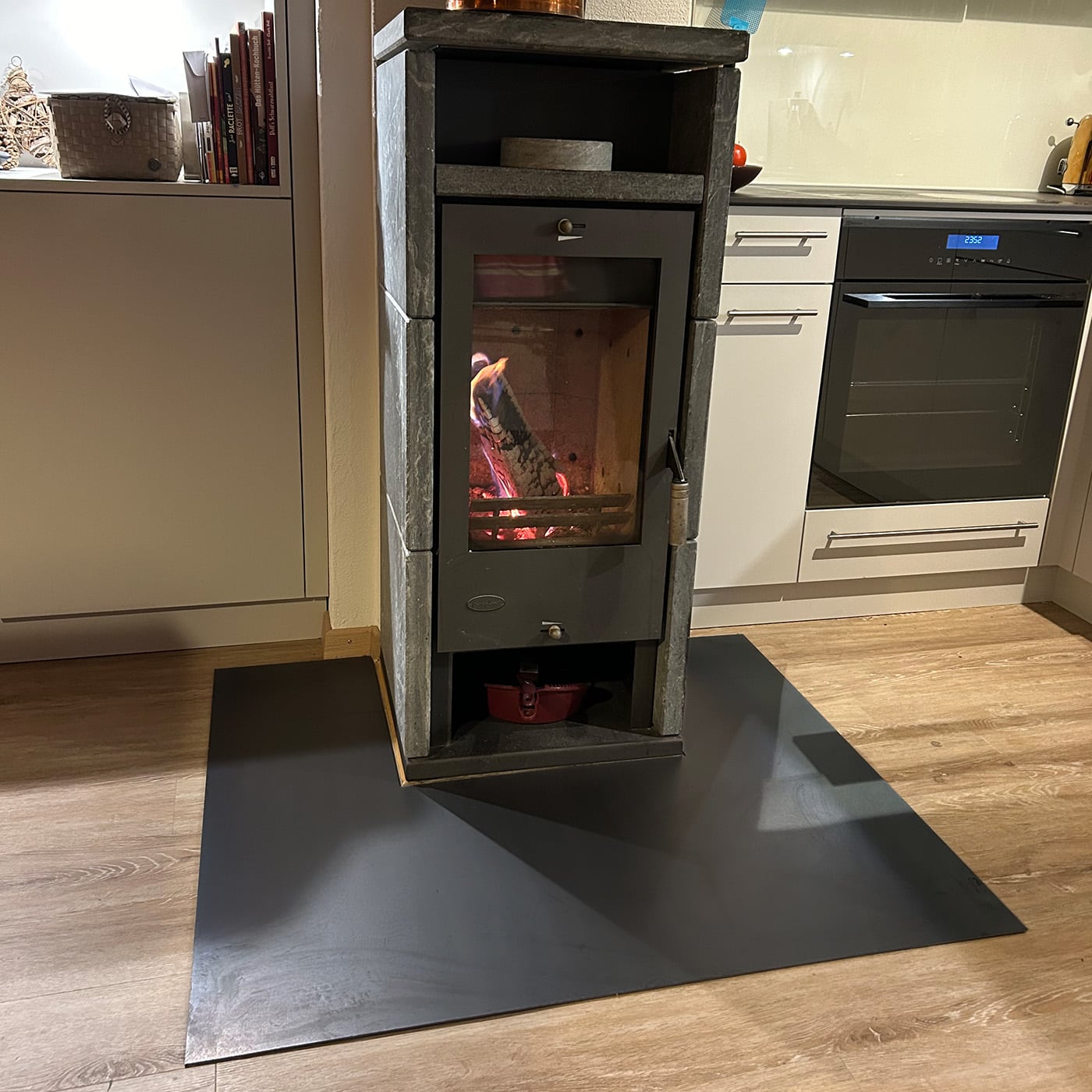 Ein Kamin steht auf einer dunklen Funkenschutz-Platte im Raum und brennt ruhig.