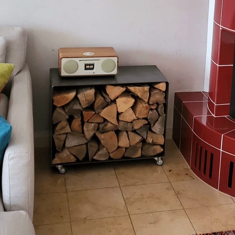 Ein Kaminholzregal steht gefüllt neben einem roten Kaminofen.