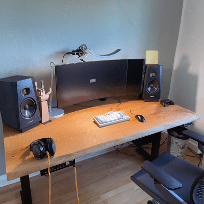 Ein Schreibtisch aus Holz steht mit Monitoren und Lautsprechern im Raum.