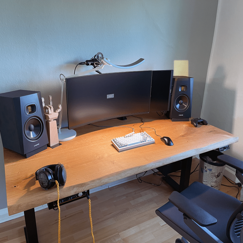 Ein Schreibtisch aus Holz steht mit Monitoren und Lautsprechern im Raum.