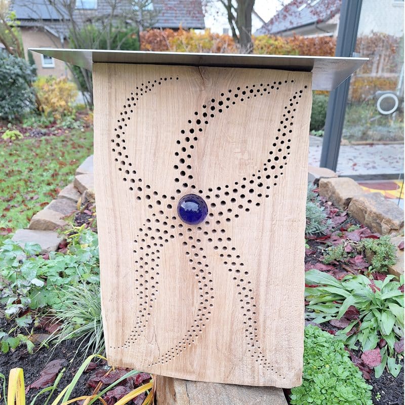 Ein dekoratives Holzelement mit Lochmuster steht in einem Garten.