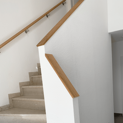 Eine Treppe mit weißer Wand und Holzhandlauf führt nach oben.