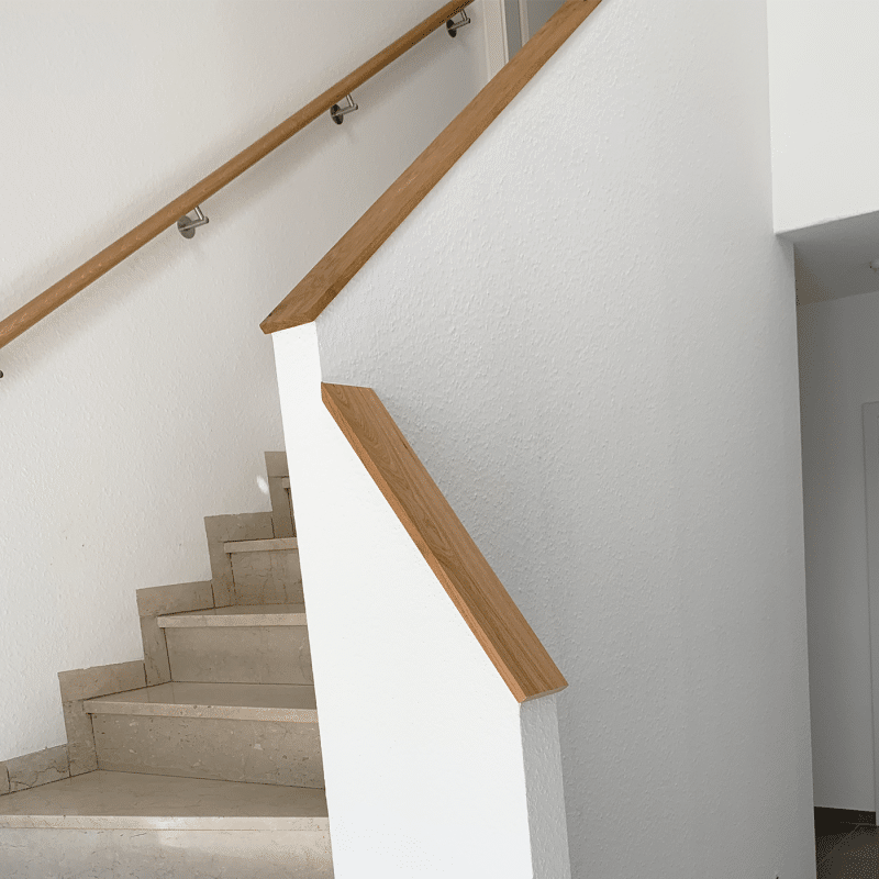Eine Treppe mit weißer Wand und Holzhandlauf führt nach oben.