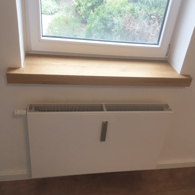 Eine Holzfensterbank sitzt passgenau über einem Heizkörper unter dem Fenster.