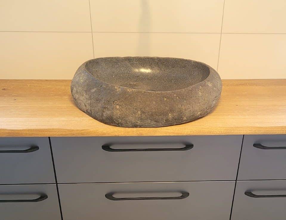 Ein rundes Steinwaschbecken steht auf einer hellen Arbeitsplatte aus Eichenholz.