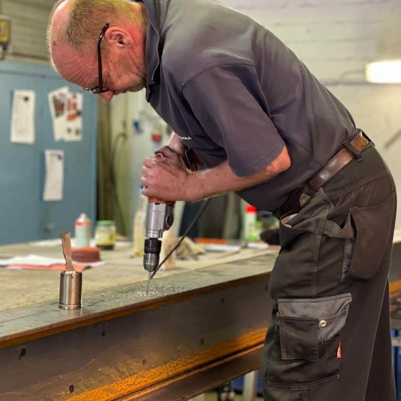 Ein Handwerker setzt eine Bohrung exakt in ein massives Metallprofil.