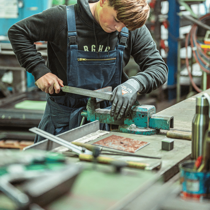 Ein Mitarbeiter bearbeitet ein Metallteil an einer Maschine in der Werkstatt.
