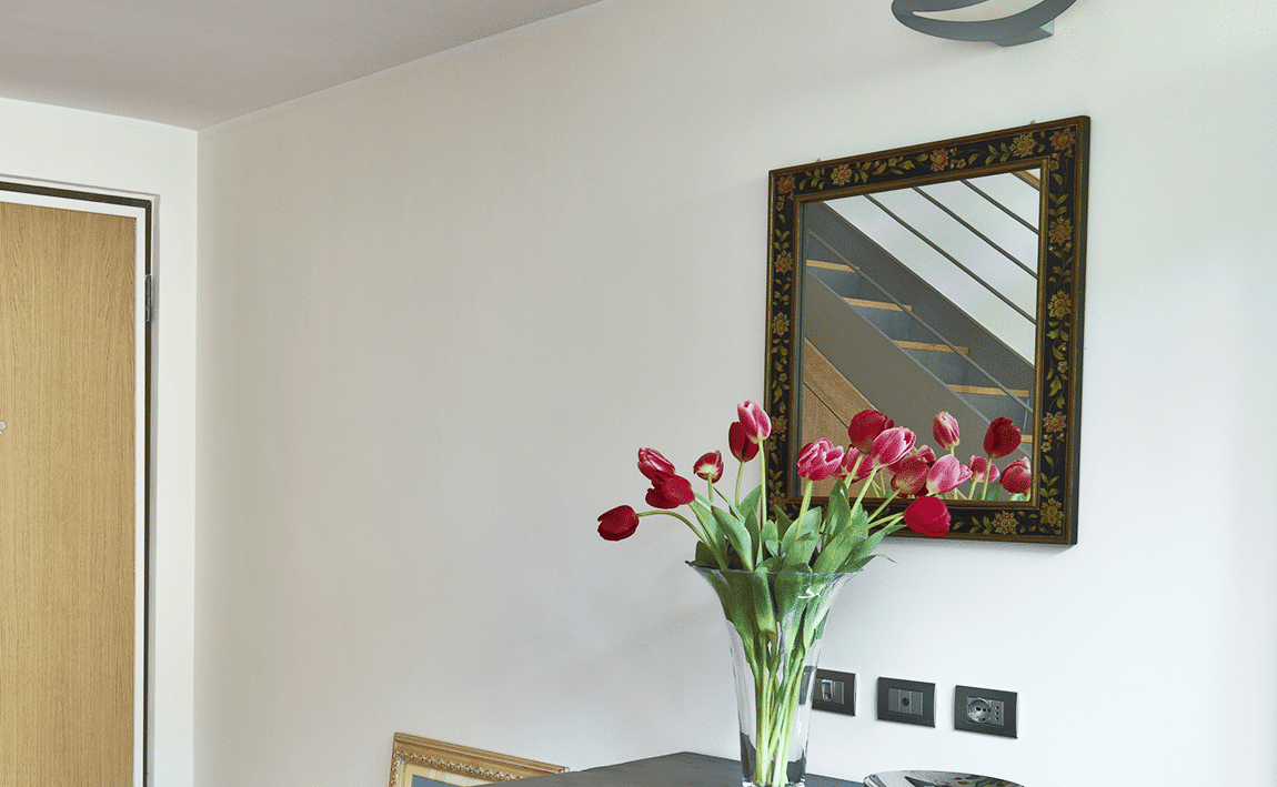 Retro-Spiegel mit floraler Holzrahmung über einer Kommode mit Tulpenvase.