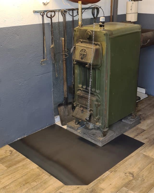 Eine schwarze Funkenschutzplatte liegt unter einer schweren Maschine aus Metall.