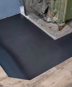 Eine schwarze Funkenschutzplatte liegt unter einer schweren Maschine aus Metall.