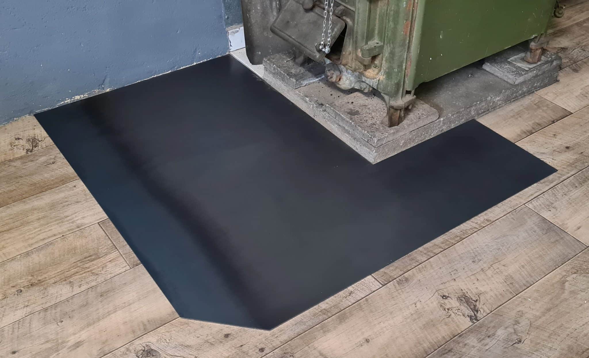 Eine schwarze Funkenschutzplatte liegt unter einer schweren Maschine aus Metall.
