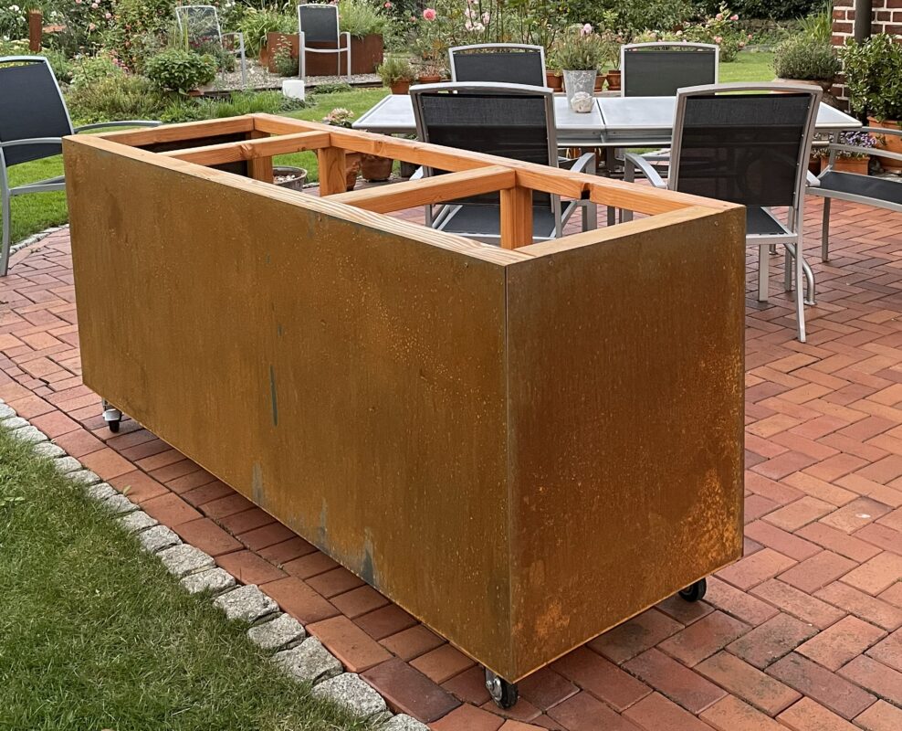 Mobile Outdoorküche mit Cortenstahl-Verkleidung, Holzrahmen und Rollen auf Terrasse.