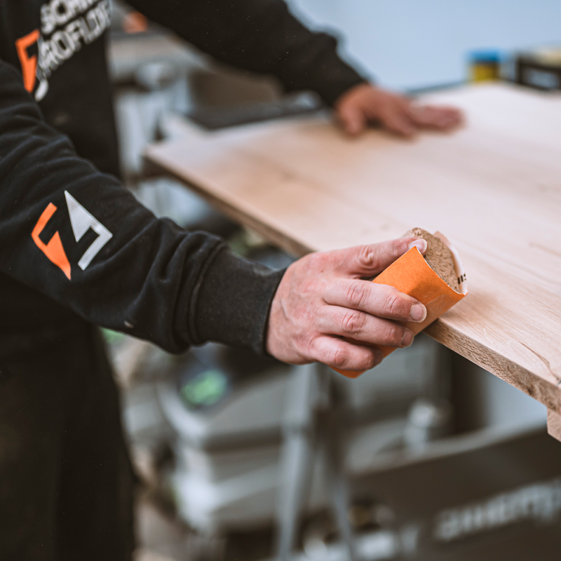 Eine Person schleift eine Holzplatte sorgfältig mit Schleifpapier von Hand.