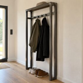 Eine schmale Garderobe aus Stahl-Quadratrohr mit Jacken und Schuhen steht neben einer schwarzen Haustür.