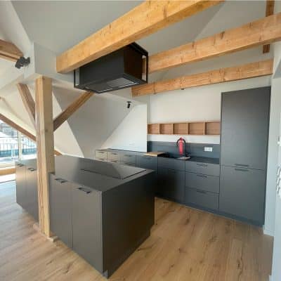Die Küche kombiniert markante Schwarzstahlflächen mit Holzbalken und wirkt modern und industriell.