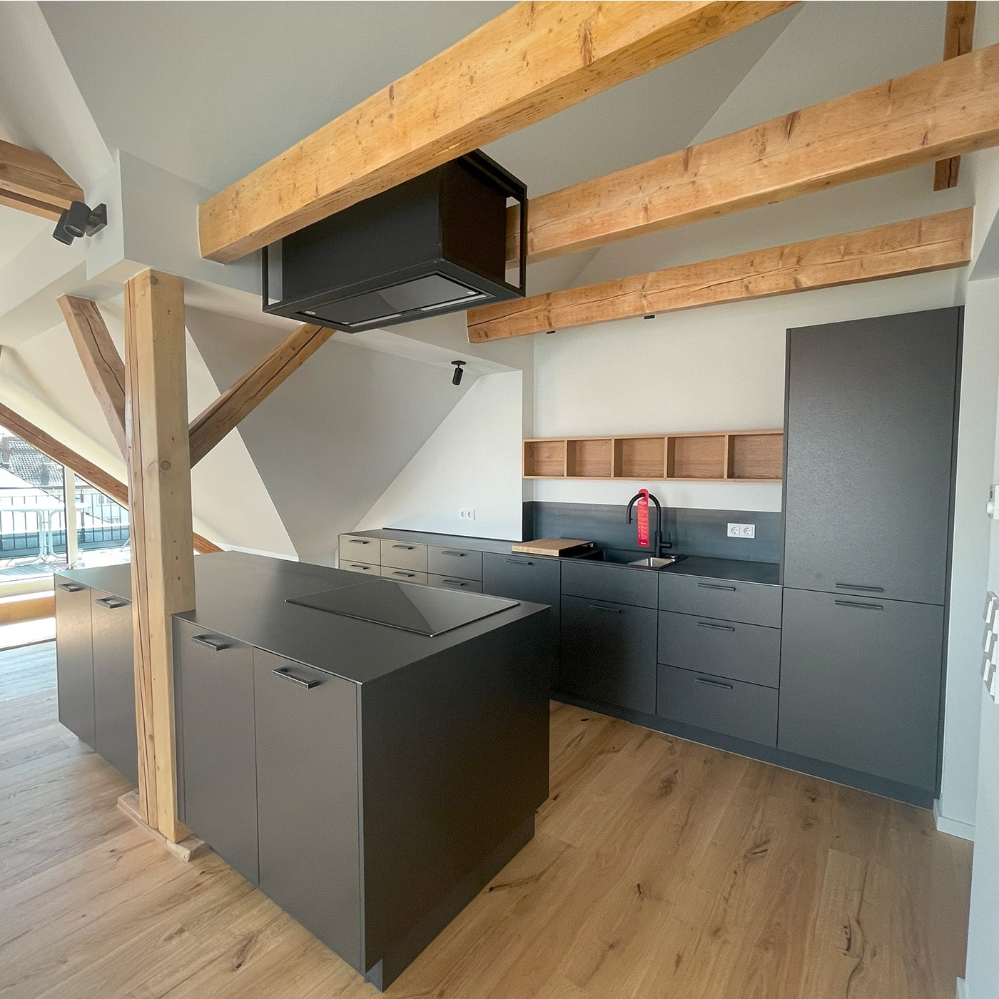 Die Küche kombiniert markante Schwarzstahlflächen mit Holzbalken und wirkt modern und industriell.