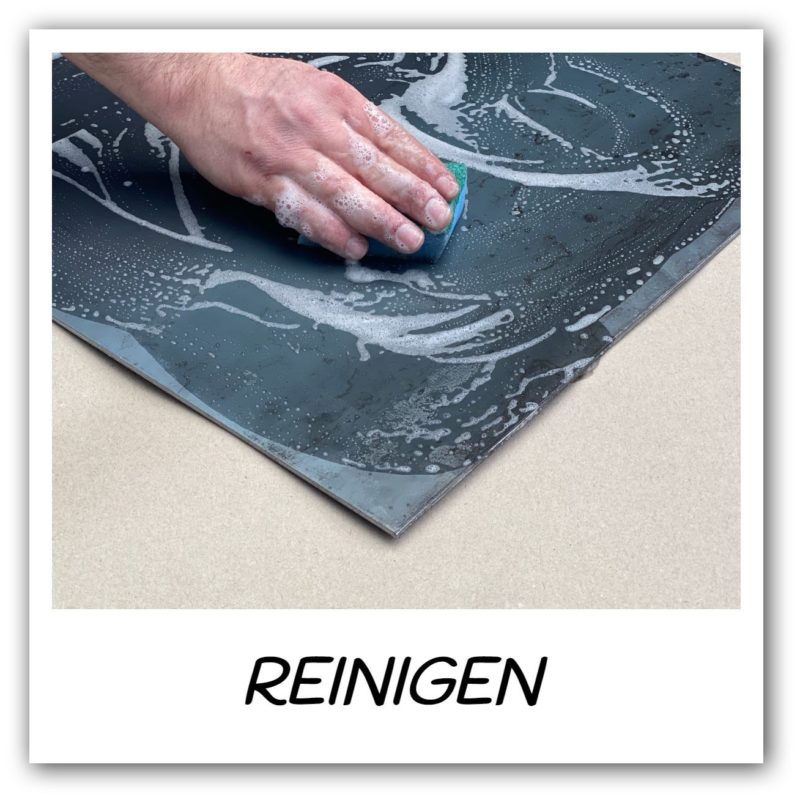 Hand reinigt eine Metallplatte mit Schwamm und Seifenwasser.
