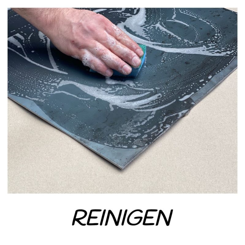 Hand reinigt eine Metallplatte mit Schwamm und Seifenwasser.