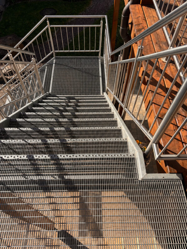 Stahltreppe mit offenen Gitterstufen ohne und seitlichem Edelstahlgeländer im Außenbereich .