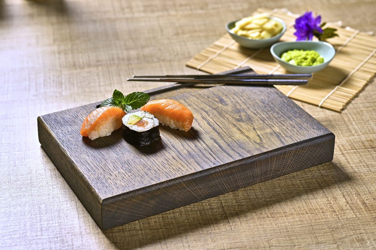 Sushi-Arrangement auf dunklem Holzbrett mit Stäbchen und Beilagen.