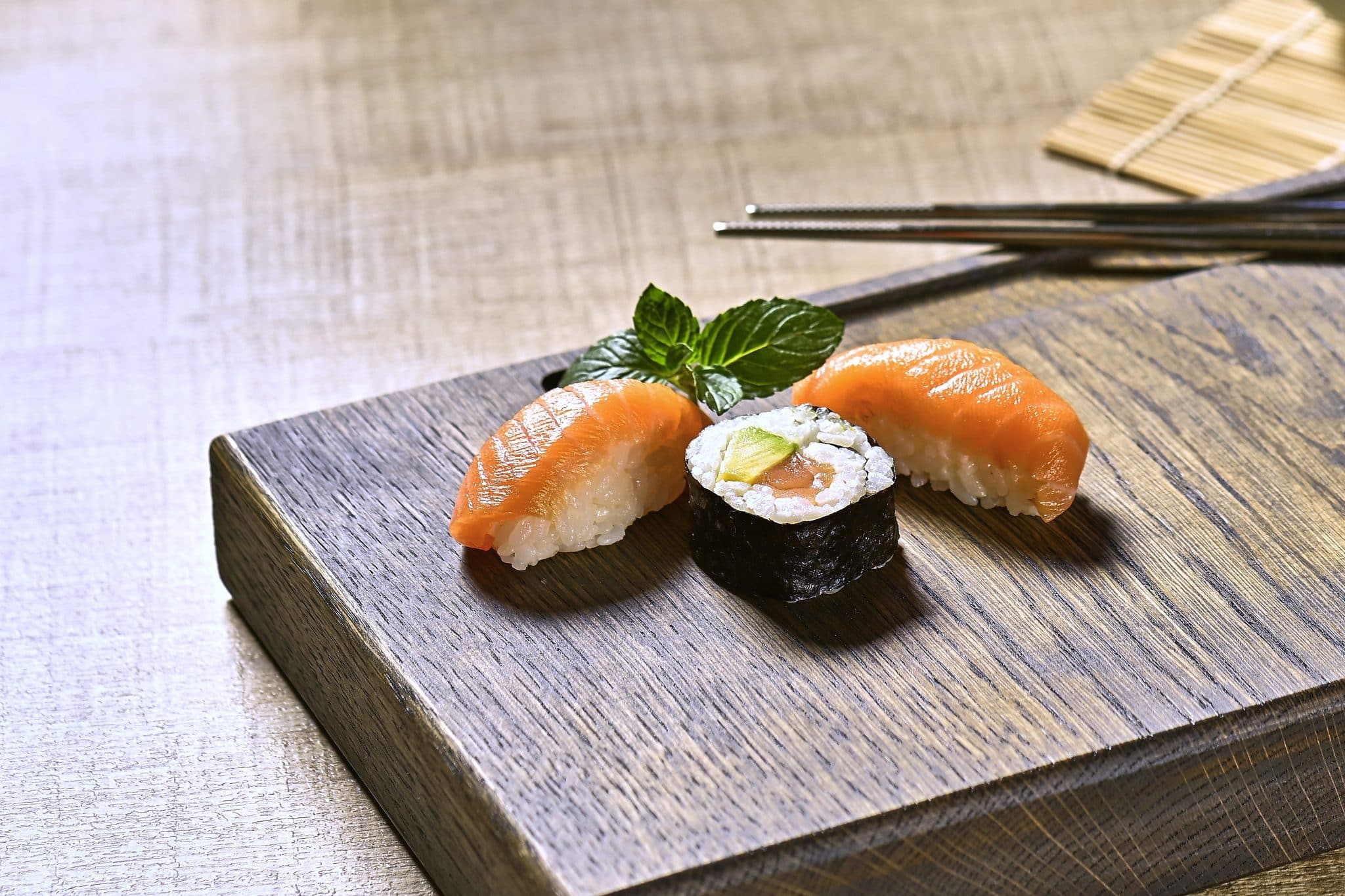 Frisches Sushi mit Lachs und einer Maki-Rolle liegt auf einem Holzbrett.