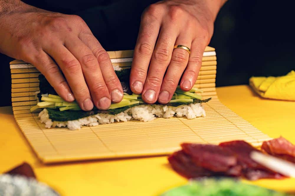 Sushizubereitung mit Bambusmatte und frischen Zutaten.