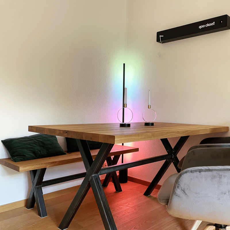 Ein Esstisch mit farbiger Lichtinstallation steht in einem Raum an der Wand.