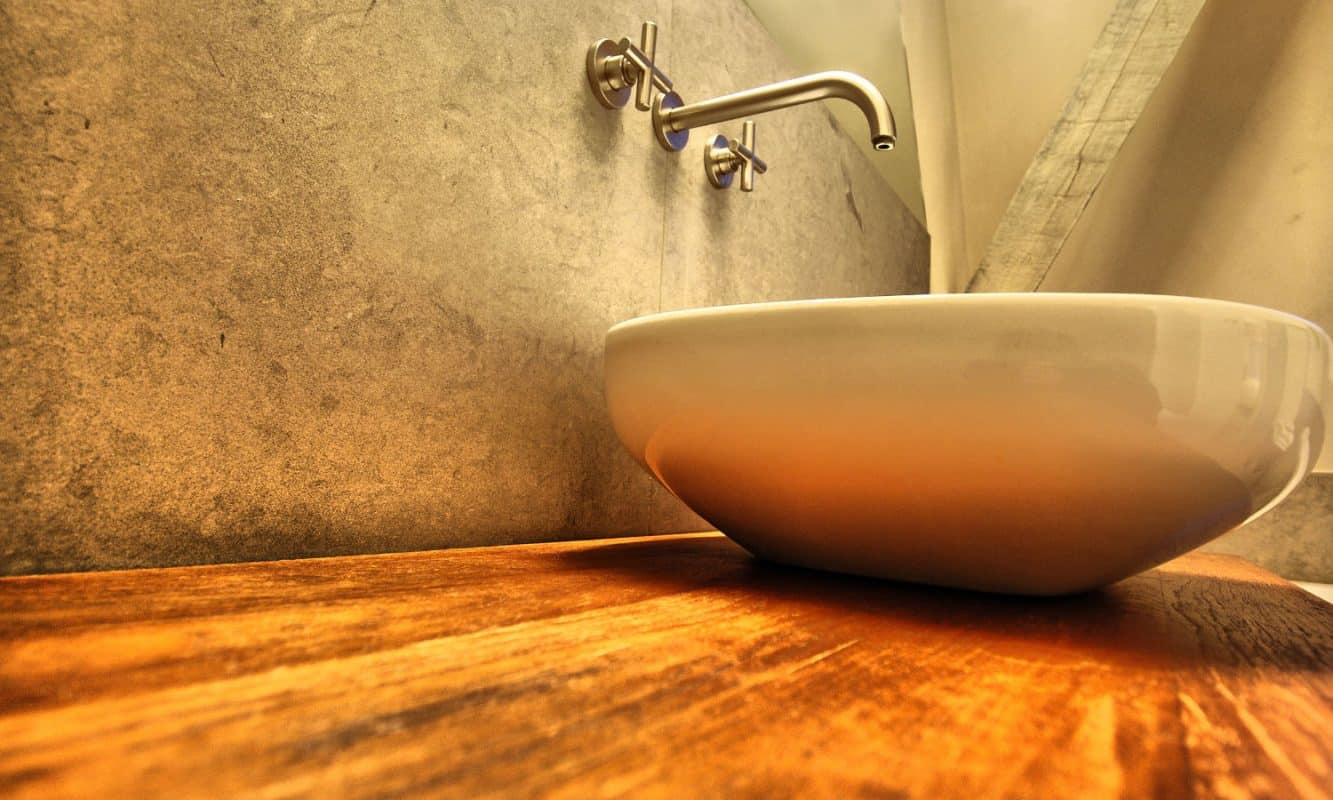 Ein Aufsatzwaschbecken steht auf einer Holzplatte vor einer warm beleuchteten Wand.
