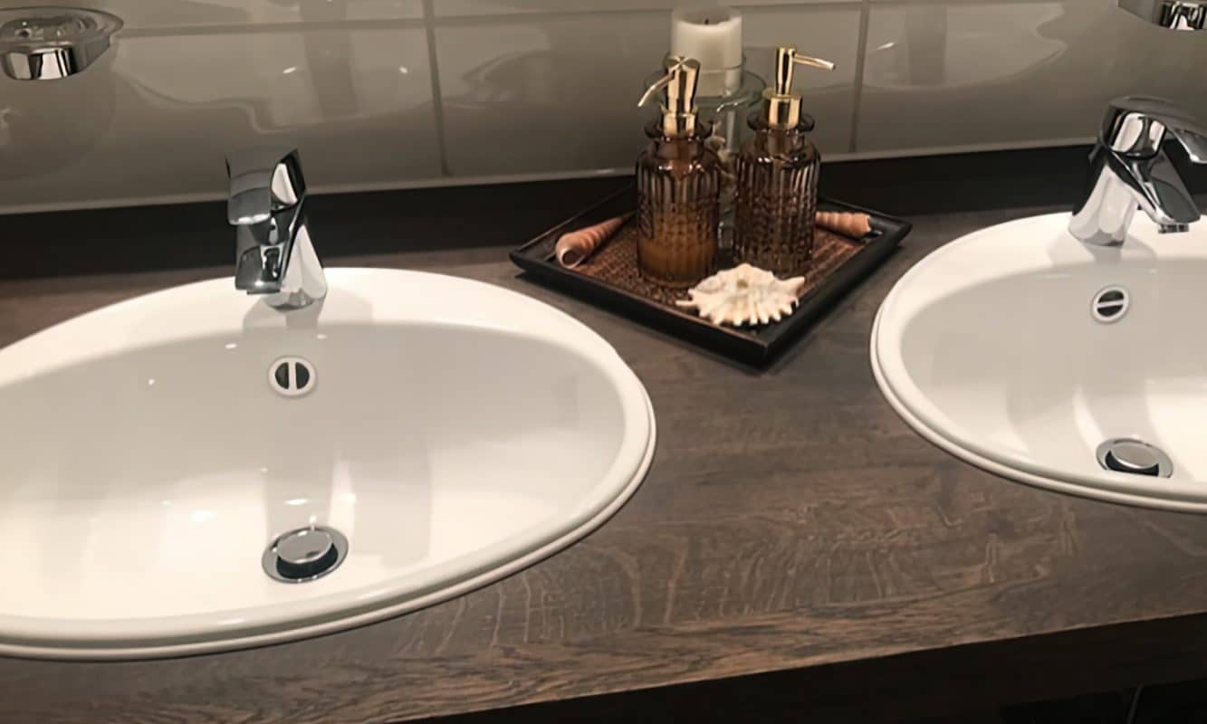 Zwei Waschbecken stehen auf einer dunklen Holzplatte mit modernen Armaturen.