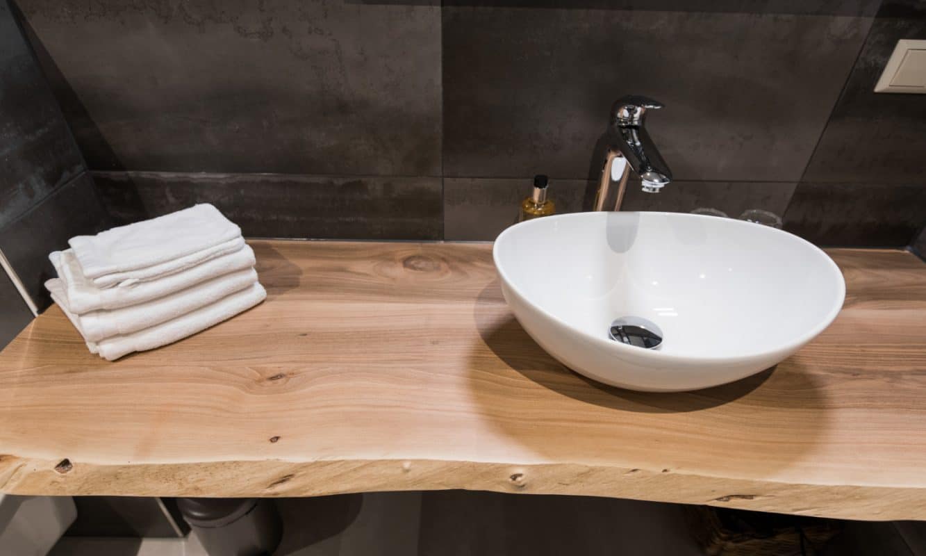 Ein weißes Waschbecken ist auf einer massiven Holzplatte montiert.