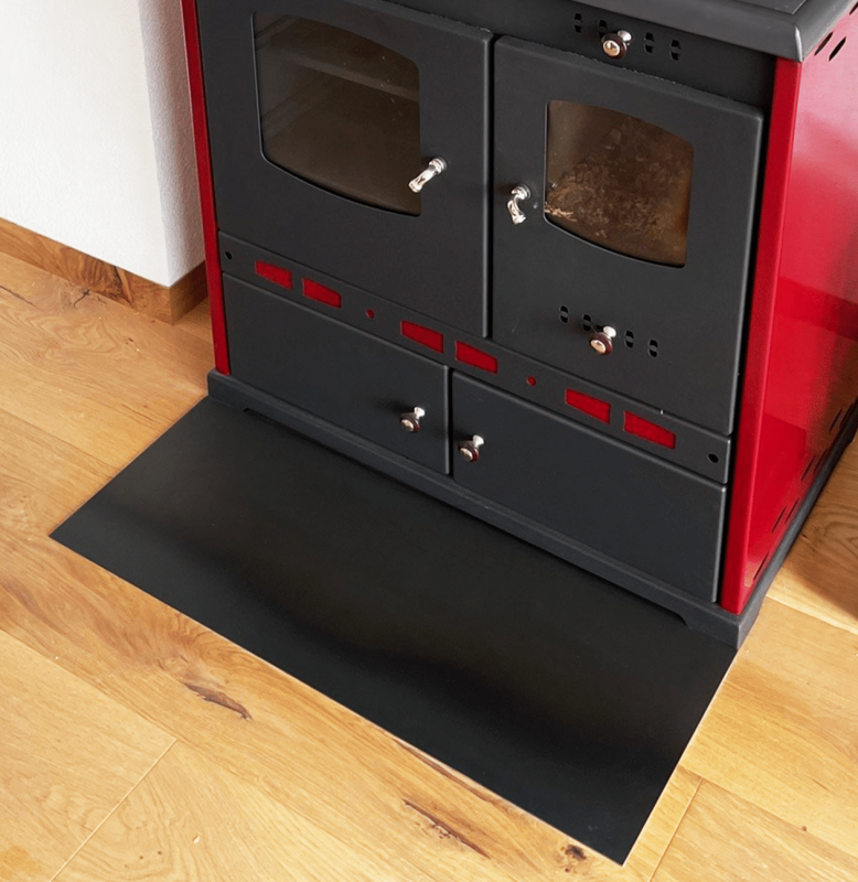 Ein schwarz-roter Kaminofen steht auf einer schwarzen Funkenschutzplatte.
