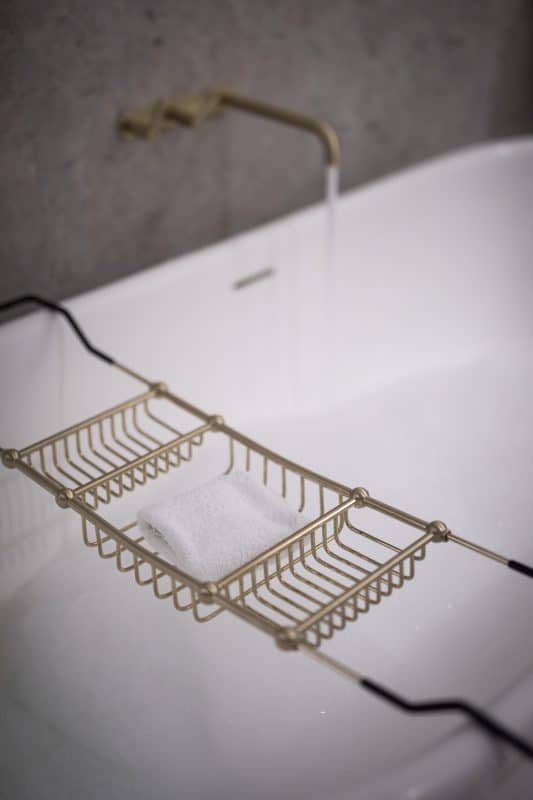 Weiße Badewanne mit goldener Armatur und Ablagekorb.
