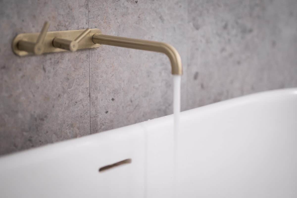Wandarmatur mit goldener Optik über weißer Badewanne.