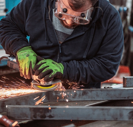 Ein Mitarbeiter von zuschnittprofi.mom schleift ein Metallstück und erzeugt dabei sichtbare Funken an der Werkbank.