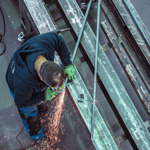 Ein Mitarbeiter von zuschnittprofi.mom arbeitet mit einem Winkelschleifer an großen Metallträgern und sorgt für saubere Schnittkanten.