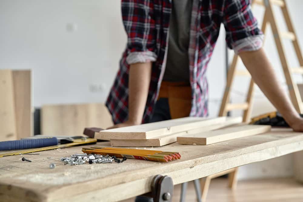 Eine Person bearbeitet Holzleisten auf einer Werkbank mit aufgelegten Werkzeugen.