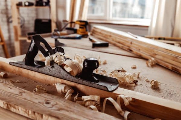 Auf einer Werkbank liegen Hobel, Holzspäne und handwerkliches Werkzeug bereit.