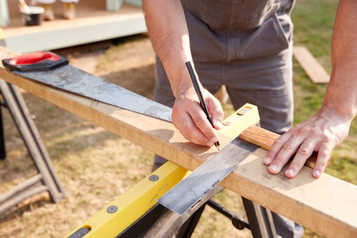 Handwerker misst und markiert Holzbrett mit Winkel und Bleistift.