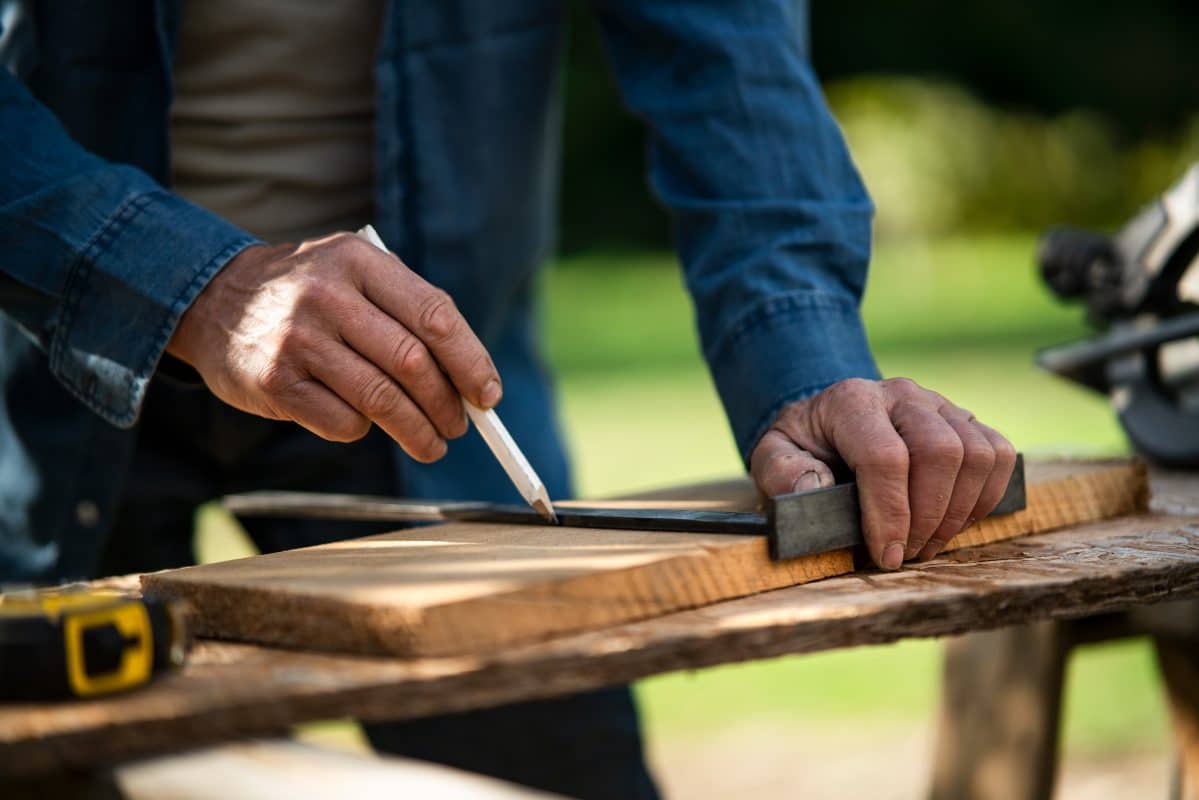 Nahaufnahme eines Handwerkers, welcher ein Holzbrett misst.