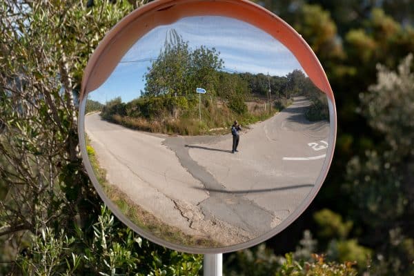 Ein runder Verkehrsspiegel reflektiert eine ruhige Straße mit Bäumen.
