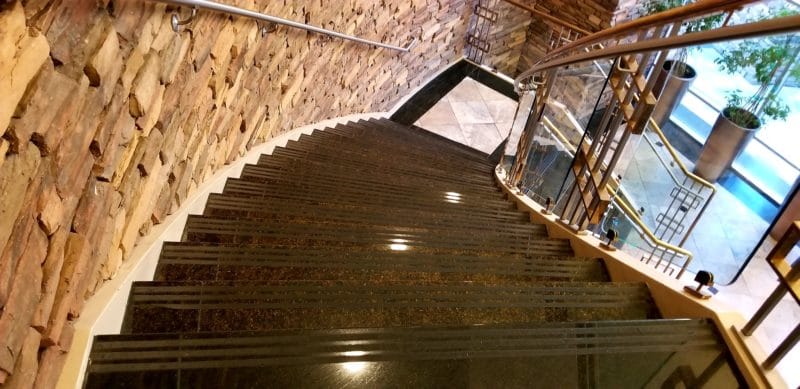 Geschwungene Treppe aus poliertem Naturstein mit Glasgeländer.