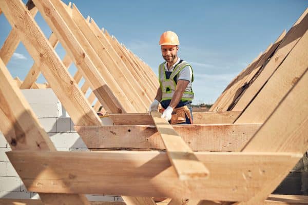 Ein Zimmermann montiert Holzbalken beim Aufbau einer Dachkonstruktion.